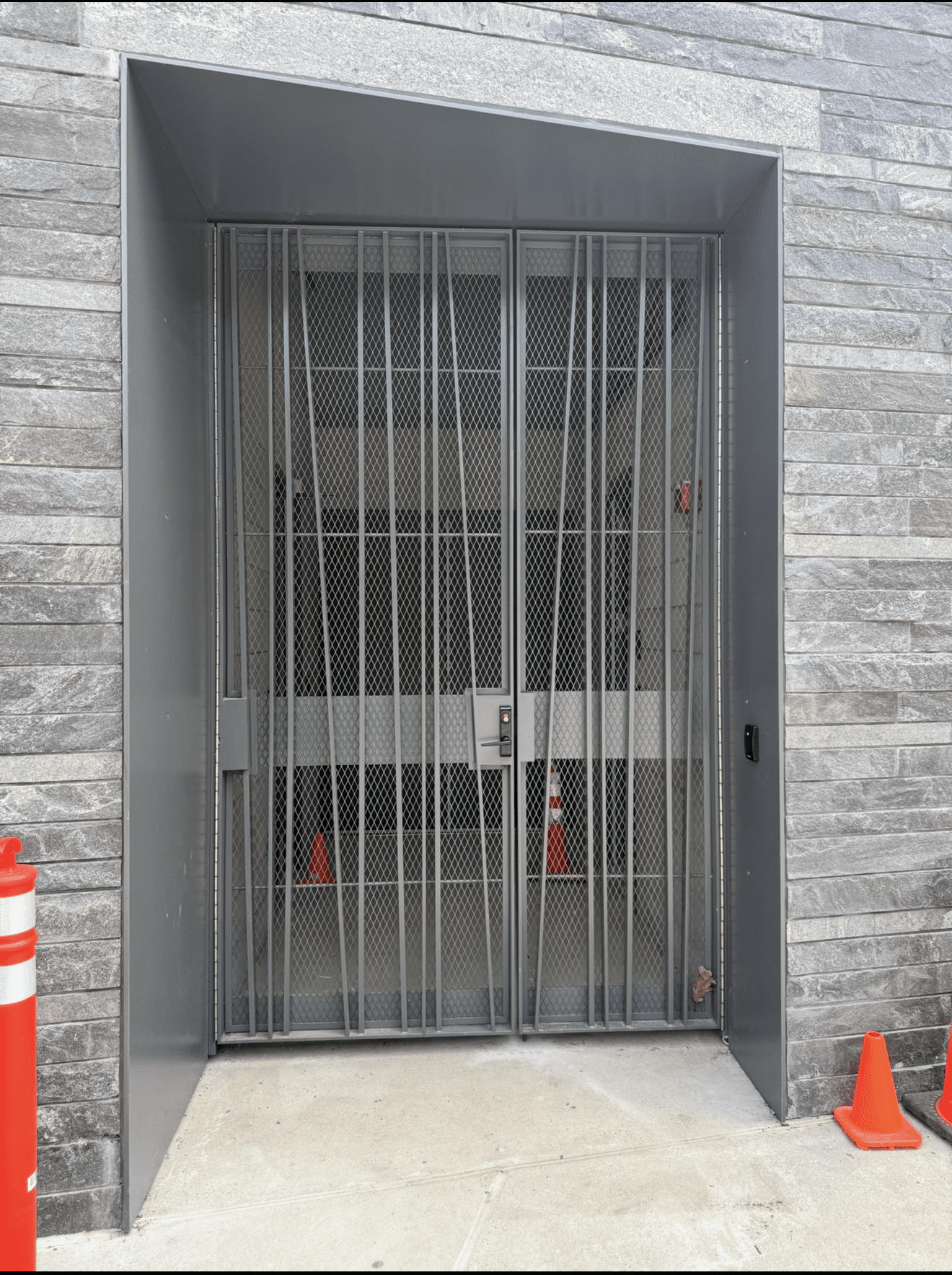 Metal gate entrance with orange traffic cones.